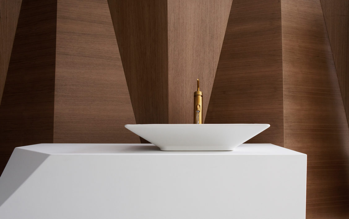 Sleek product photography of a white Kohler sink and wood paneling background.