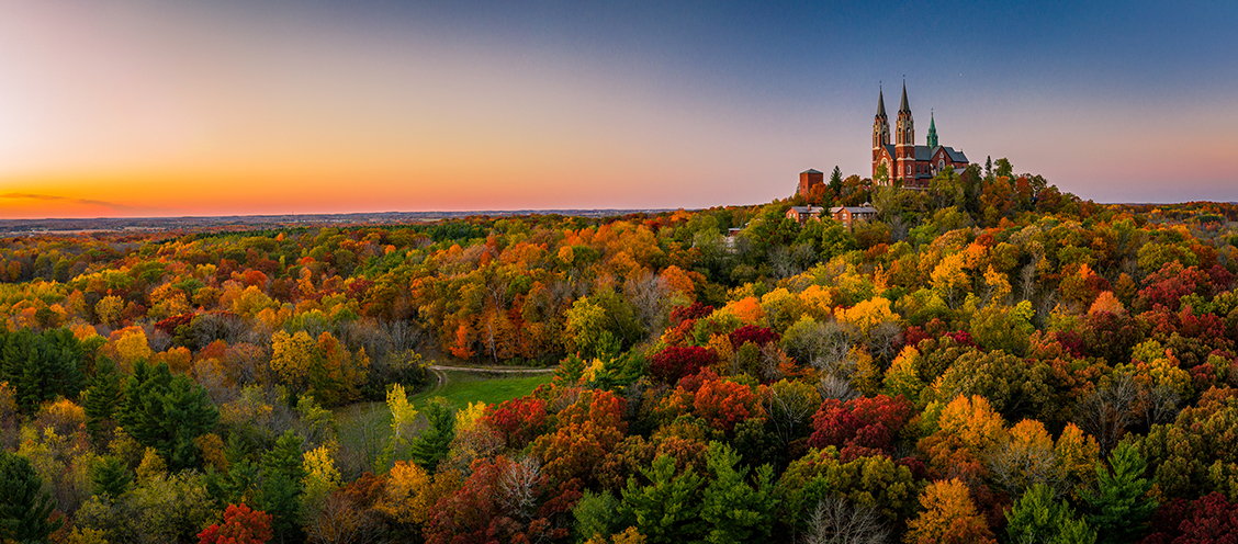 Panoramic drone photograph of trees in fall and a large building on a hill